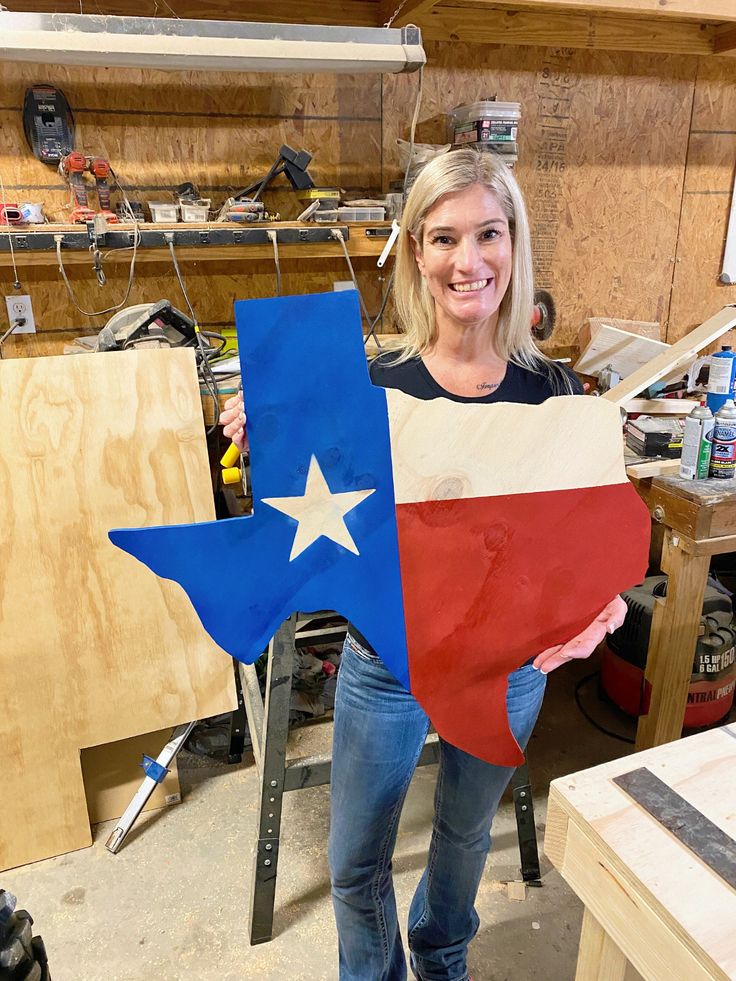 a woman holding up a large texas flag cut out of plywood in a workshop