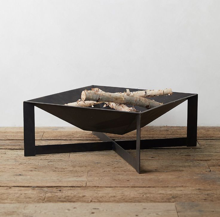 a square fire pit sitting on top of a wooden floor next to a white wall