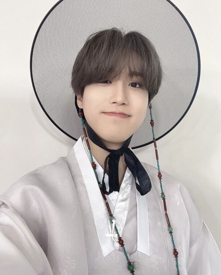 a person wearing a hat and necklace with beads on it's neck, standing in front of a white wall