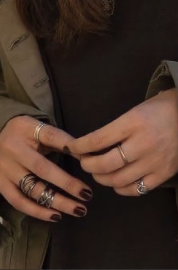 the woman is holding her hands together with different rings on their fingers and wearing a trench coat