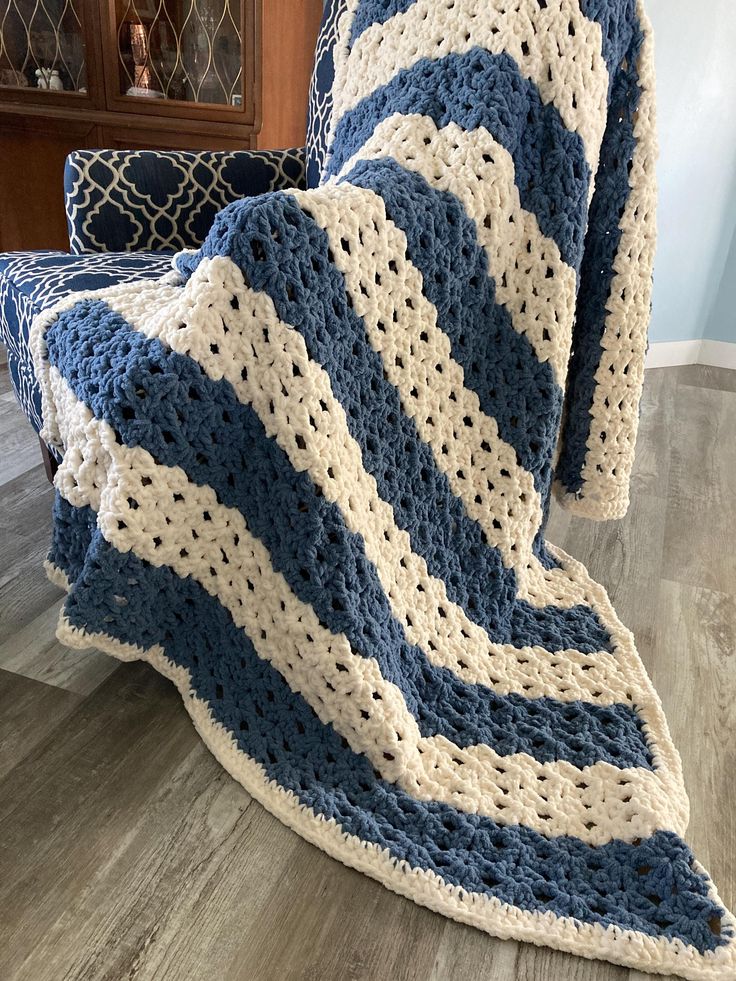 a blue and white crocheted blanket sitting on top of a wooden floor next to a chair