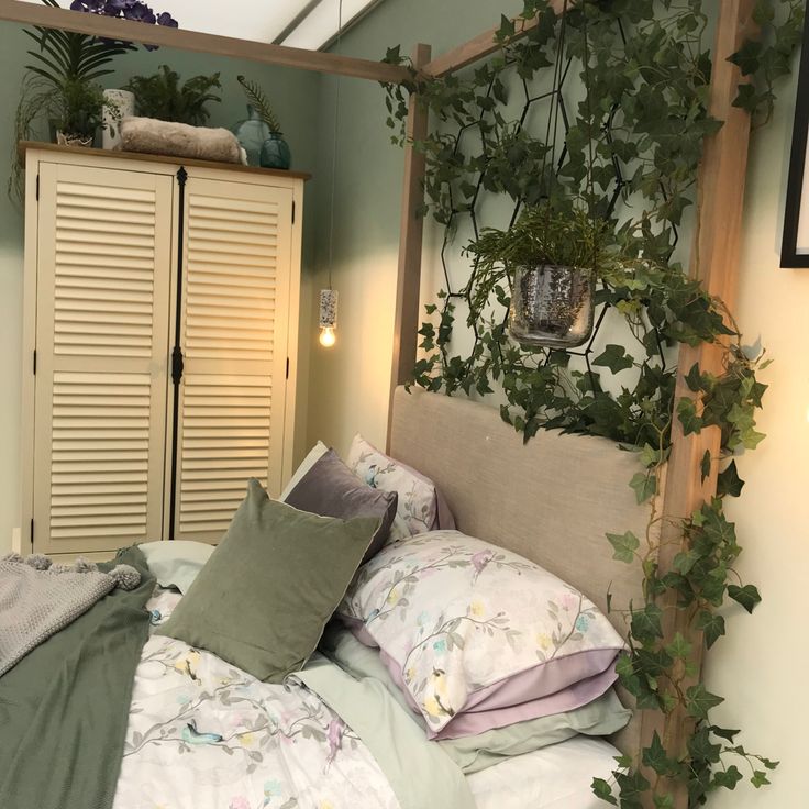 a bed with lots of pillows and plants on it's headboard in a bedroom