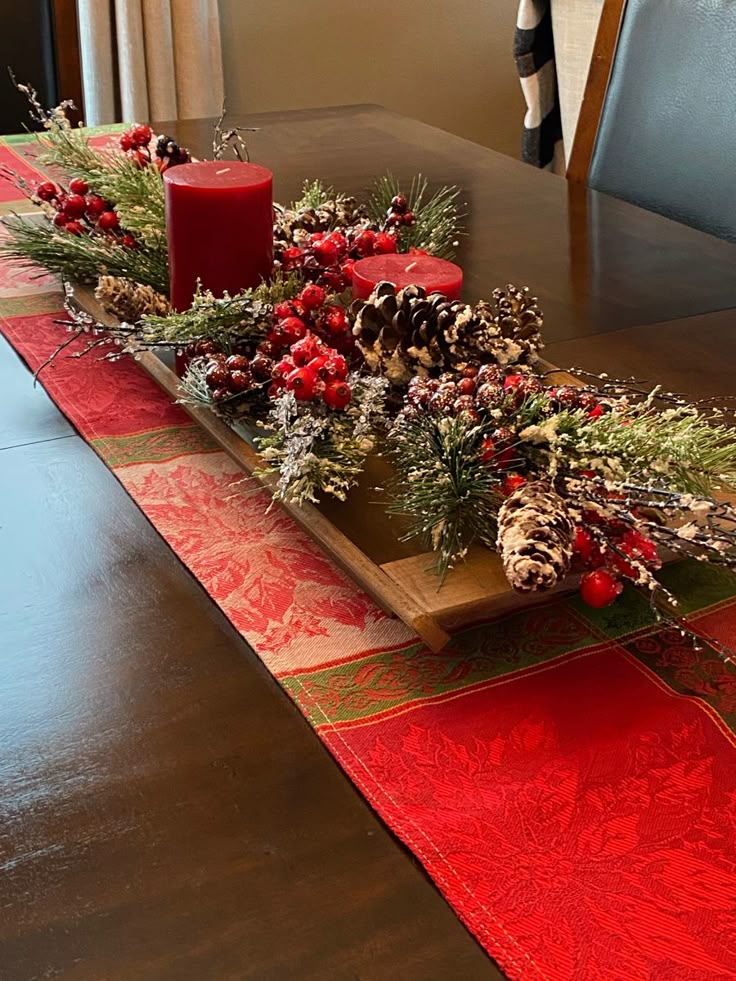 a wooden table topped with red candles and greenery next to a christmas centerpiece