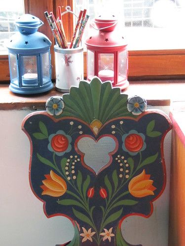 an ornate wooden sign with flowers and hearts painted on it's side in front of a window