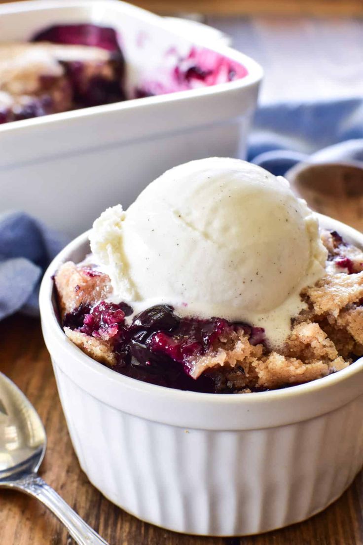 a scoop of ice cream sits on top of a blueberry cobbler in a white bowl