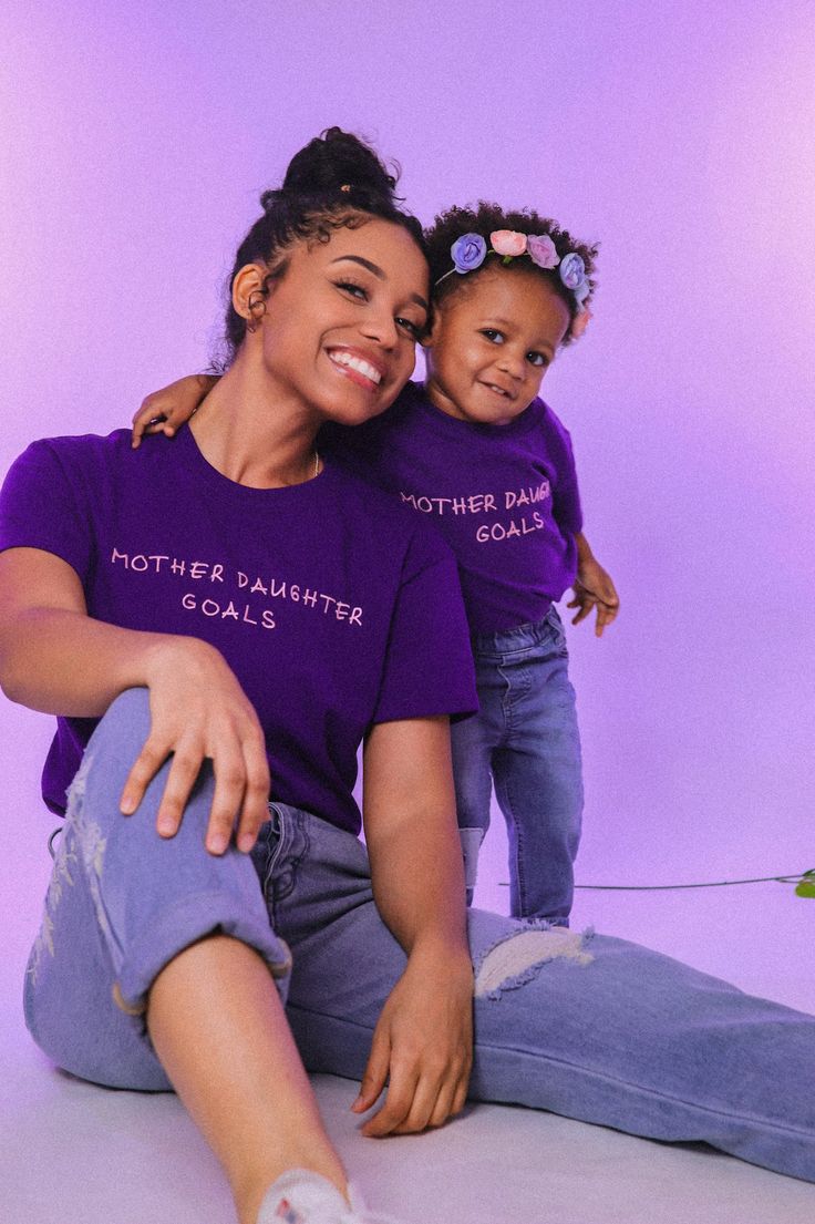 a mother and daughter sitting on the floor together, wearing matching purple t - shirts