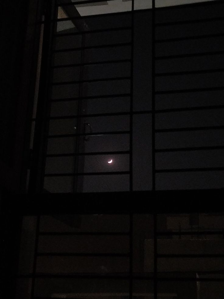 the moon is seen through an open window in this dark night time scene, with only one light visible