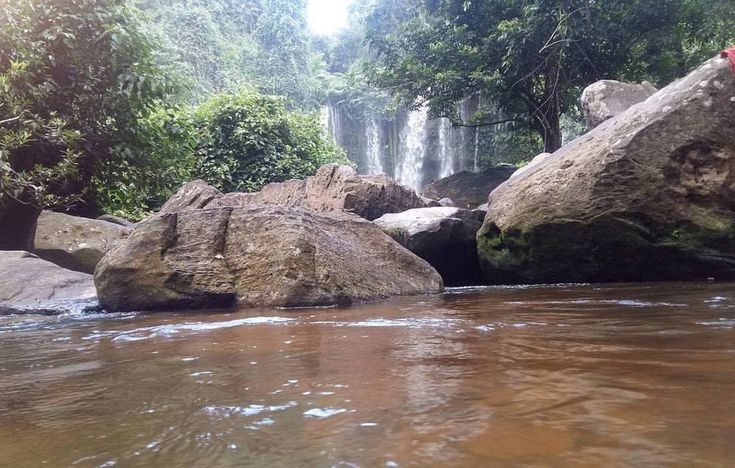 some rocks in the middle of a body of water with a waterfall in the background