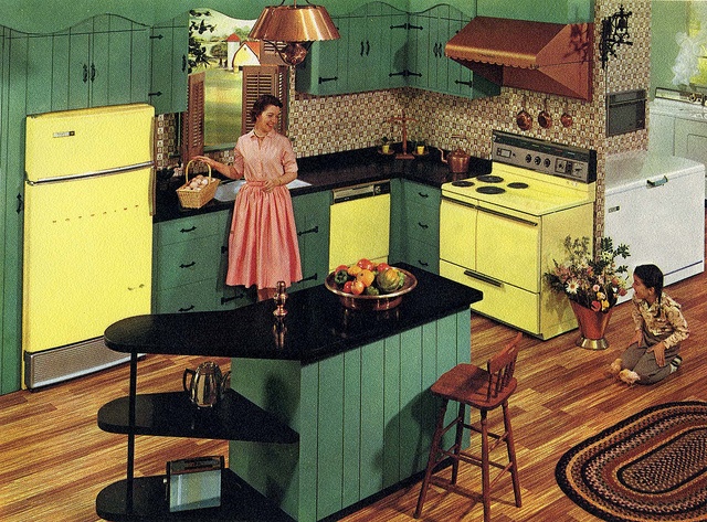 a woman standing in the middle of a kitchen with yellow cabinets and black counter tops