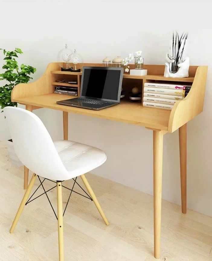 a laptop computer sitting on top of a wooden desk next to a white chair and potted plant