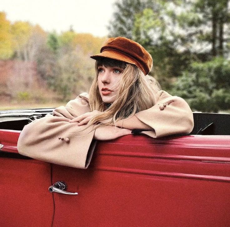 a woman leaning on the hood of an old red car with her arms folded out