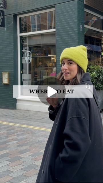 a woman walking down the street in front of a store with a yellow hat on