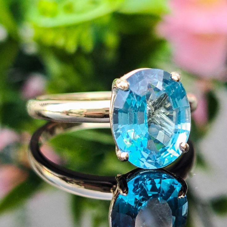 two rings with blue topaz and white bottomaz on each one, sitting in front of flowers