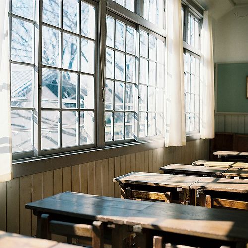 an empty classroom with wooden desks and windows