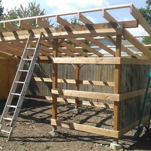 a wooden structure with a ladder attached to it and a shed in the back ground