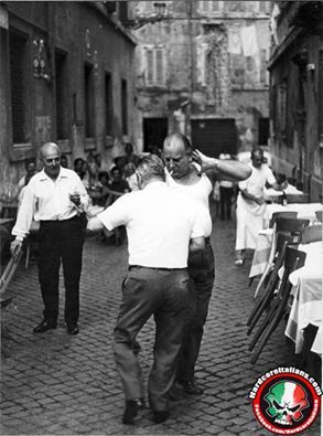 an old black and white photo of two men dancing in the middle of a cobblestone street