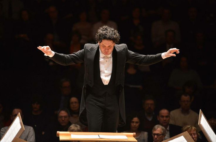 conductor in black suit standing on stage with arms outstretched