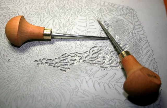 a pair of scissors cutting wood on top of a piece of paper with intricate designs