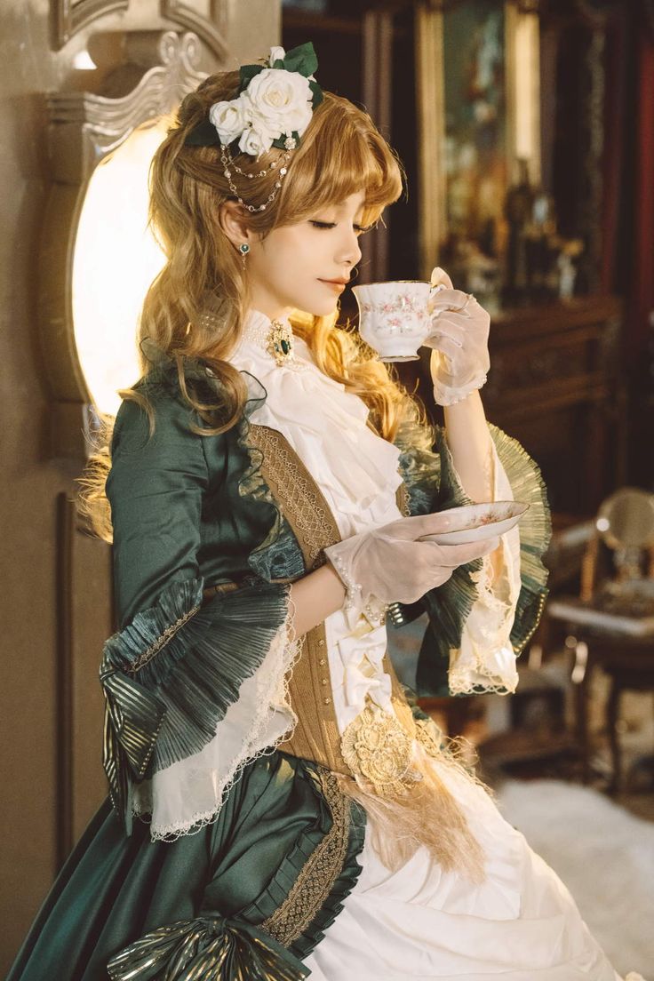 a woman dressed in green and white is holding a tea cup with her right hand