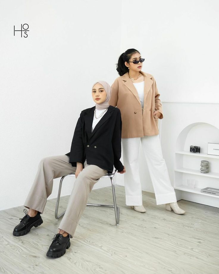 two women sitting on chairs in front of a white wall