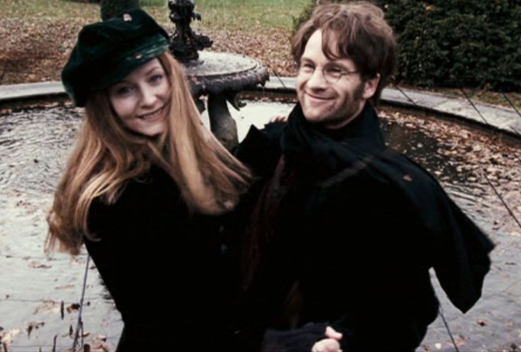 a man and woman standing next to each other in front of a train track with trees