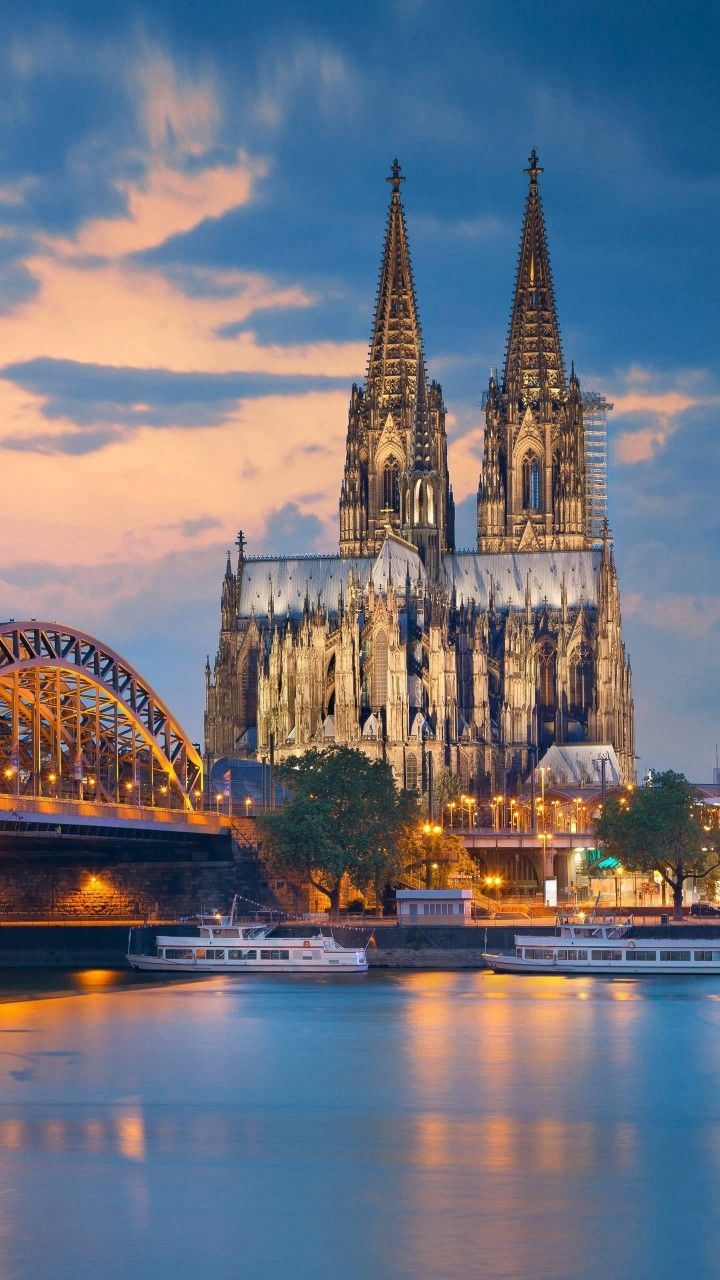 a large cathedral towering over a city next to a body of water at dusk with boats in the foreground