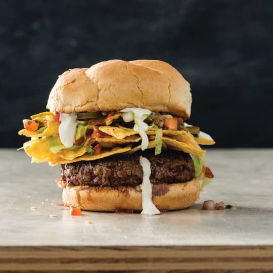 a hamburger with cheese, lettuce and other toppings sitting on a table