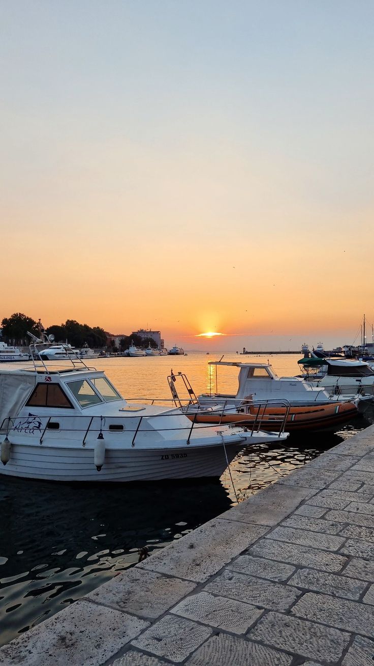 several boats are docked in the water at sunset