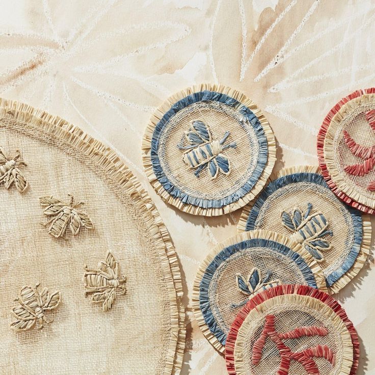 four embroidered coasters with bees on them sitting on a white cloth covered tablecloth