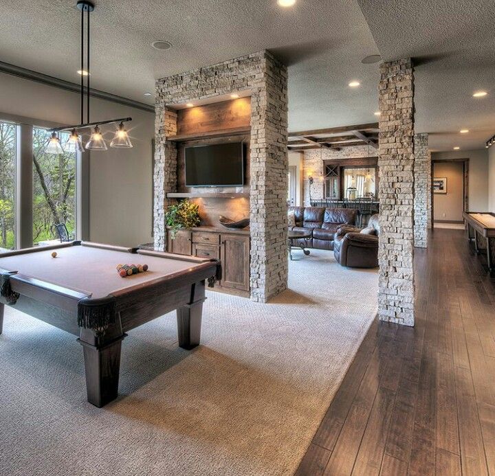 a pool table in the middle of a living room with large windows and stone columns