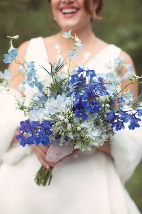 a woman in a white dress holding a bouquet of blue flowers and smiling at the camera