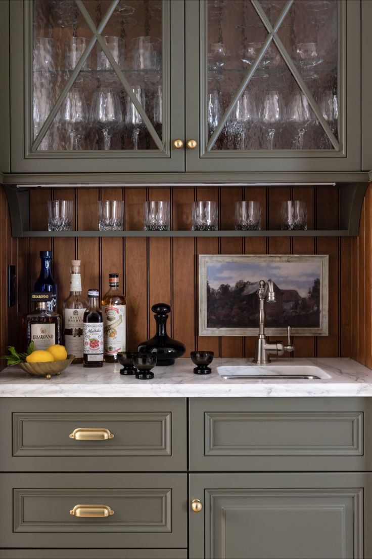 a kitchen cabinet with wine glasses and liquor bottles on it's front, next to a sink