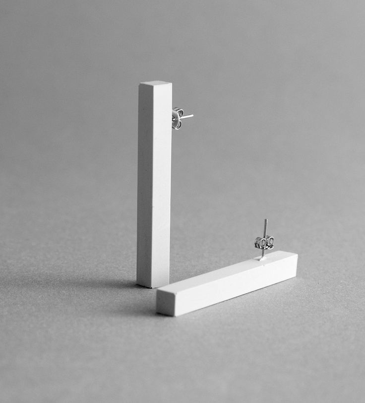 a pair of earrings sitting on top of a white piece of wood in front of a gray background