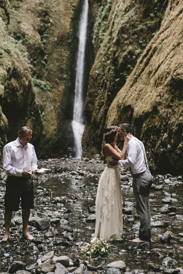 a bride and groom standing in front of a waterfall during their elopetion ceremony