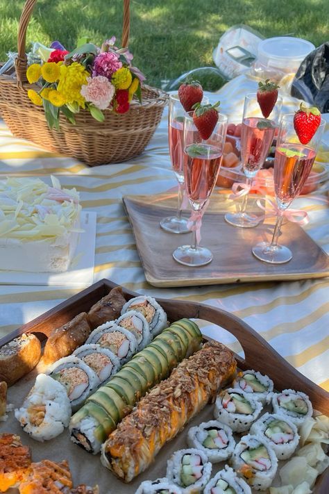 an assortment of sushi and wine on a picnic table with flowers in the background