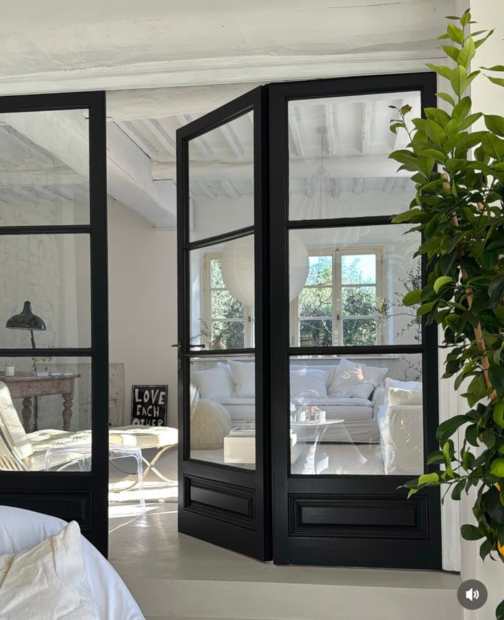 an open door leading to a living room with white furniture and plants in the corner