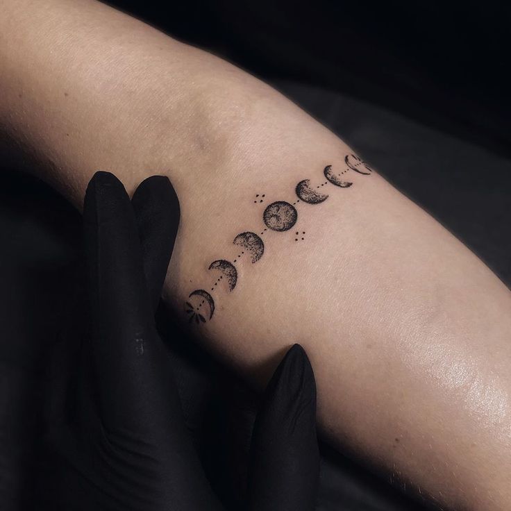 a woman's arm with phases of the moon tattooed on her left arm and black gloves