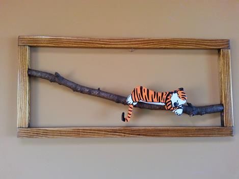 a wooden frame with a stuffed tiger on it's side hanging from a tree branch