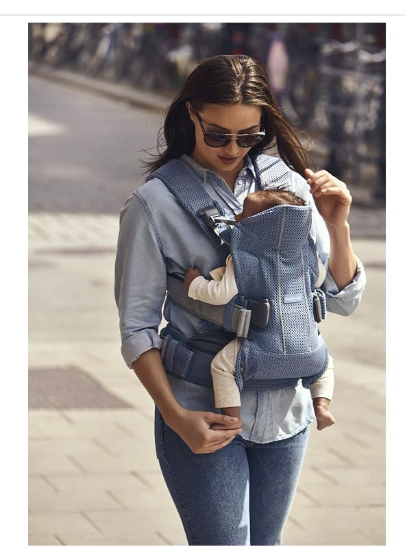 a woman walking down the street with her baby in a carrier on her back and wearing sunglasses