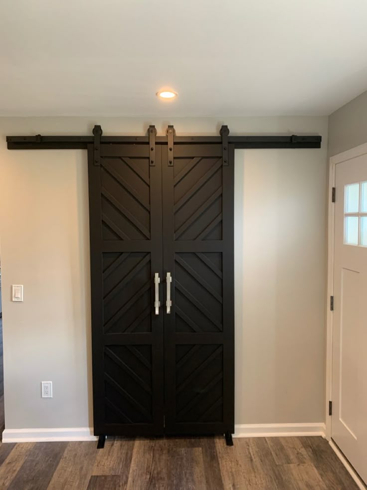 an empty room with two black doors and wood flooring on either side of the door