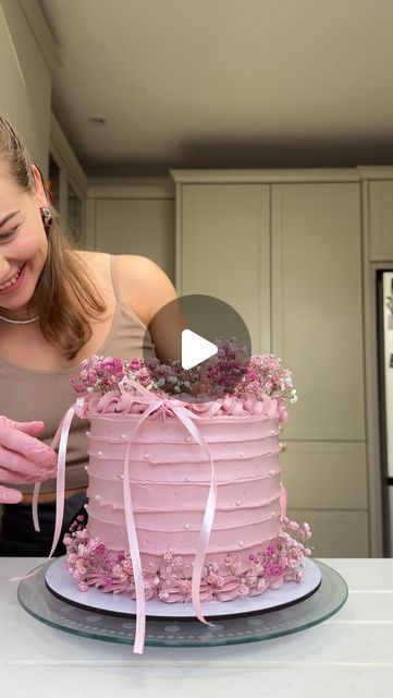 a woman is decorating a pink cake