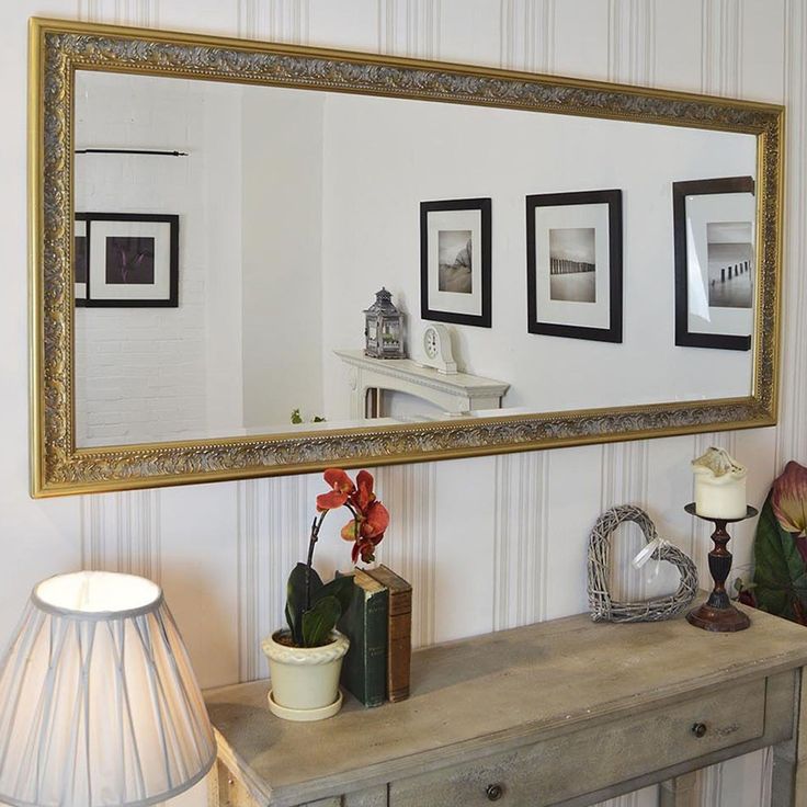 there is a large mirror on the wall above a table with flowers and other decorations