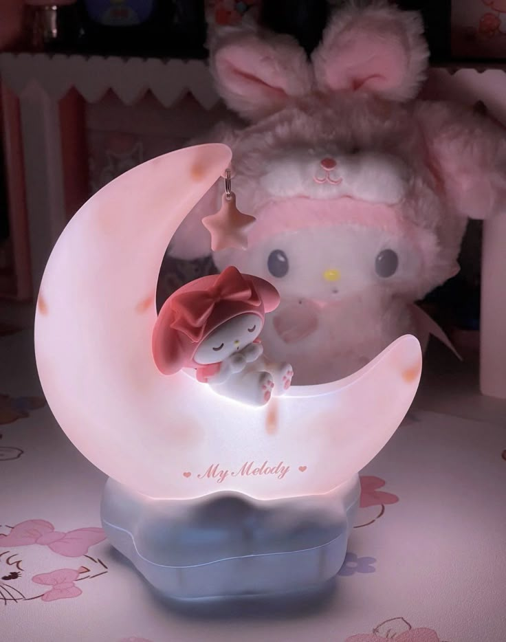 a pink stuffed animal sitting on top of a moon shaped night light in a room