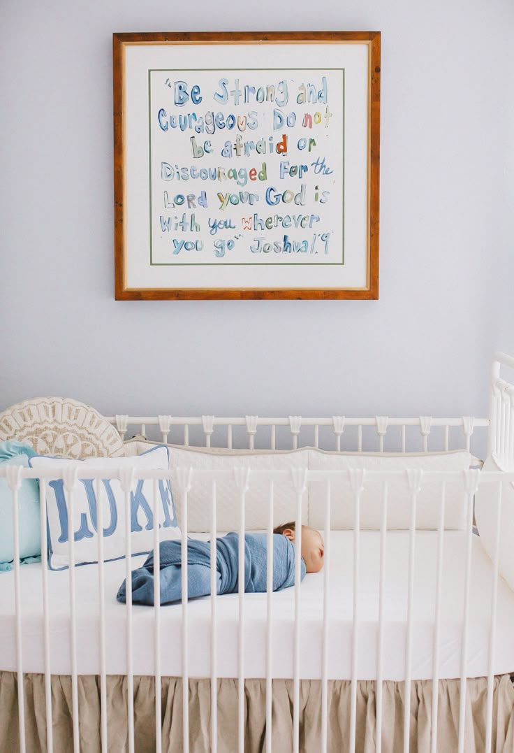 a baby is laying in his crib next to a framed print on the wall