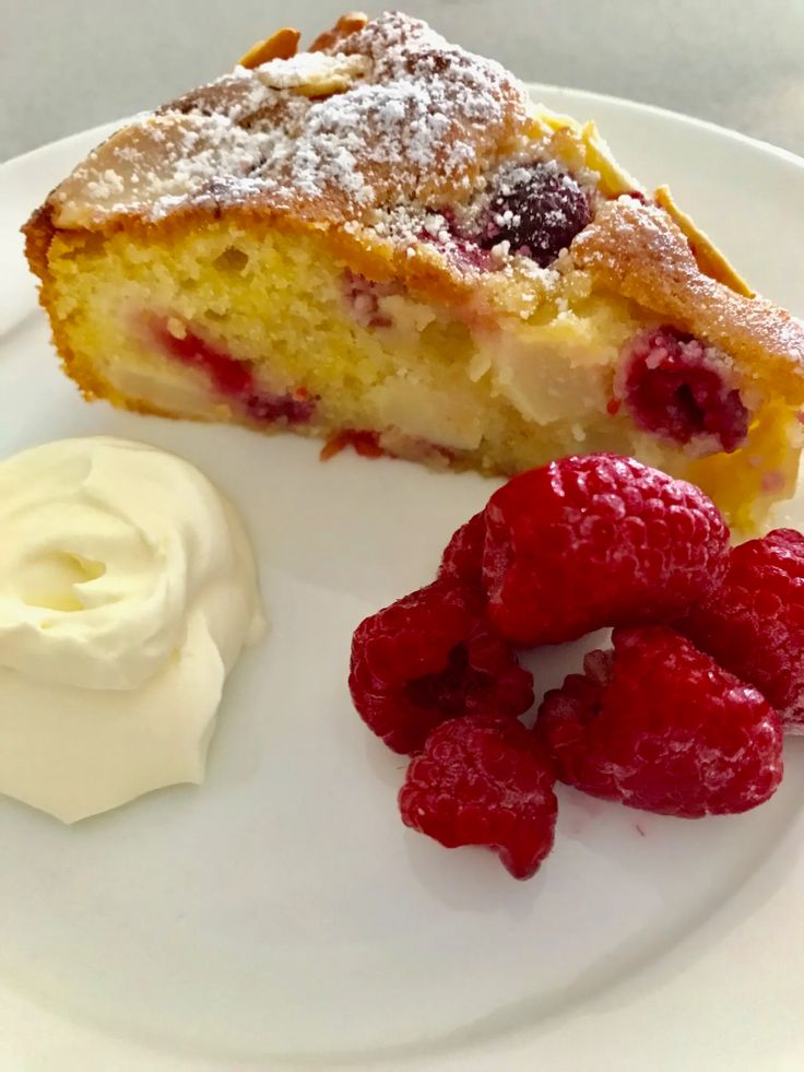 a piece of cake and some raspberries on a white plate with whipped cream