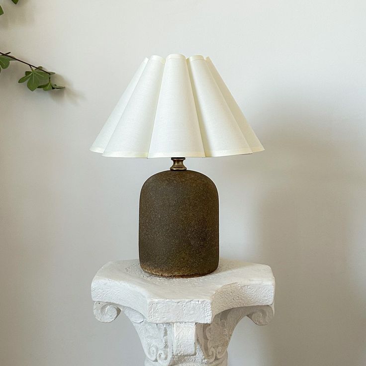 a lamp sitting on top of a white table next to a wall with a plant