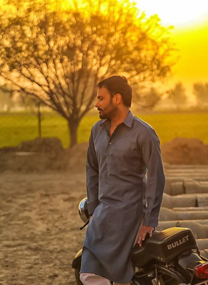 a man standing next to a motorcycle in front of a field with grass and trees