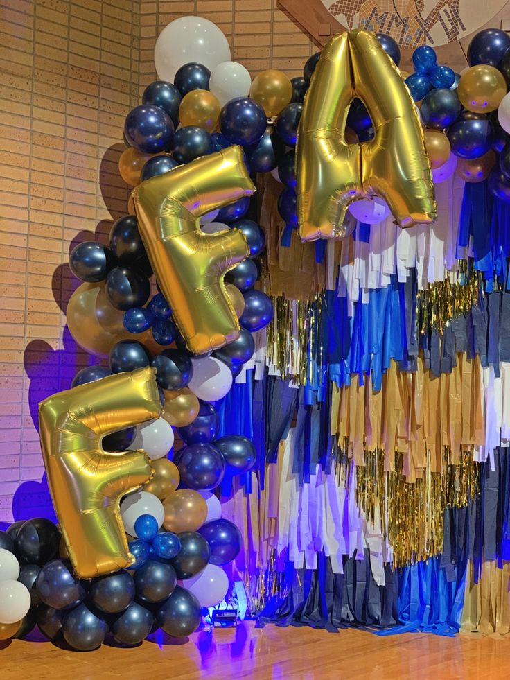 balloons and streamers in the shape of letters are displayed on a table with blue, gold and white decorations