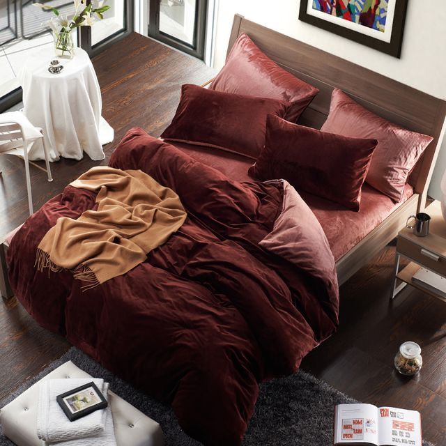 a bed with red sheets and pillows on top of it in a room next to a table