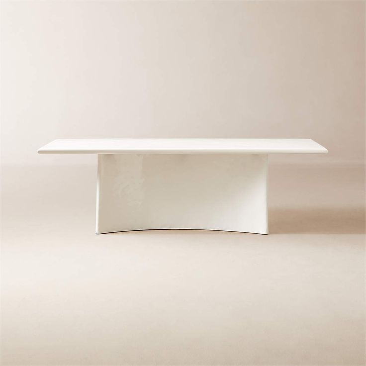 a white table sitting on top of a floor next to a beige wall and chair